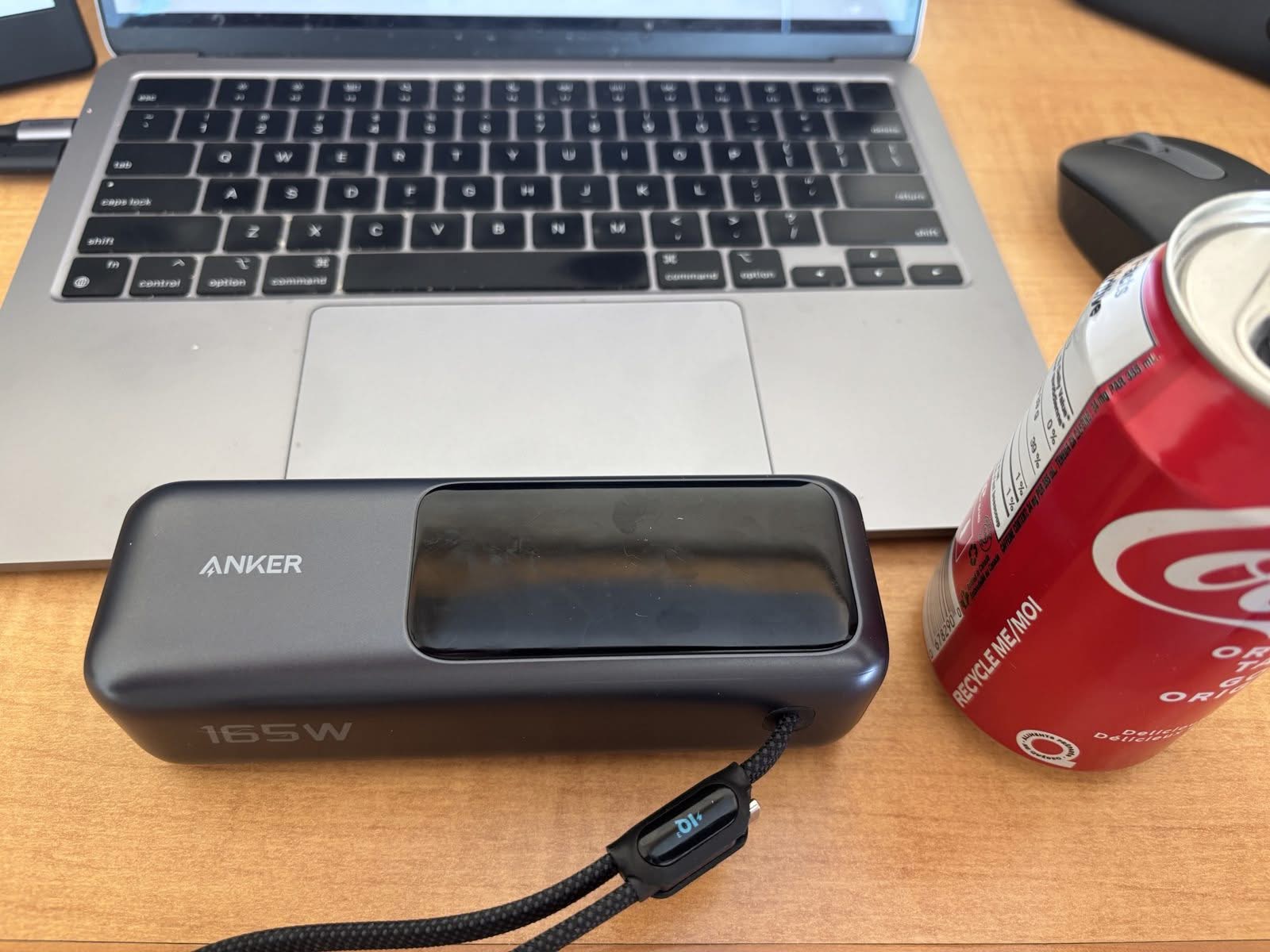 Anker 25,000mAh laptop power bank with its built-in braided USB-C cable, sitting in front of a MacBook Air